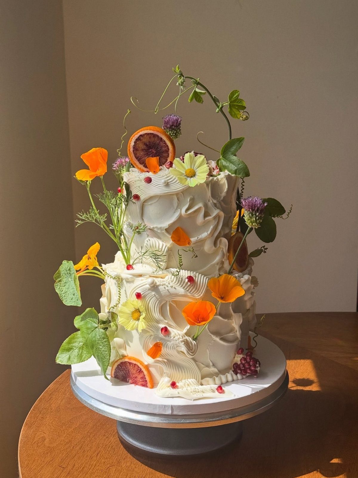 Two-tier white frosted cake decorated with spring flowers and dried citrus slices.