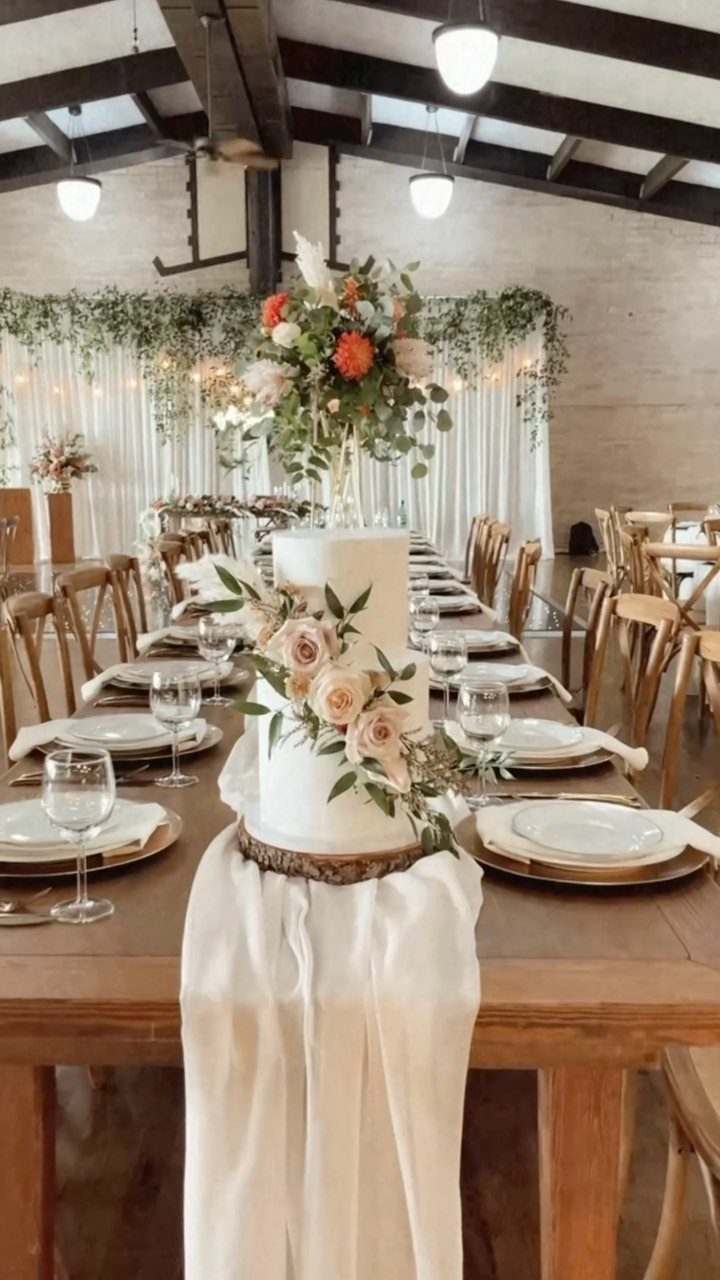 Two-tier white wedding cake with pink roses on a rustic wooden slice base.