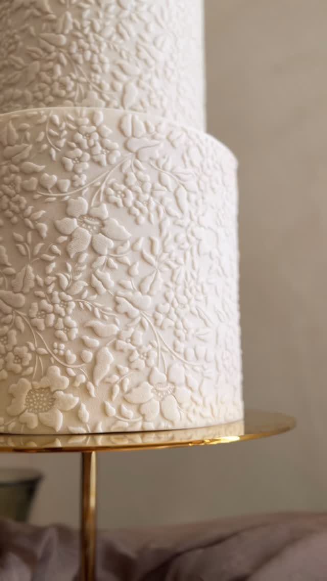 White tiered cake with embossed floral patterns on a gold cake stand