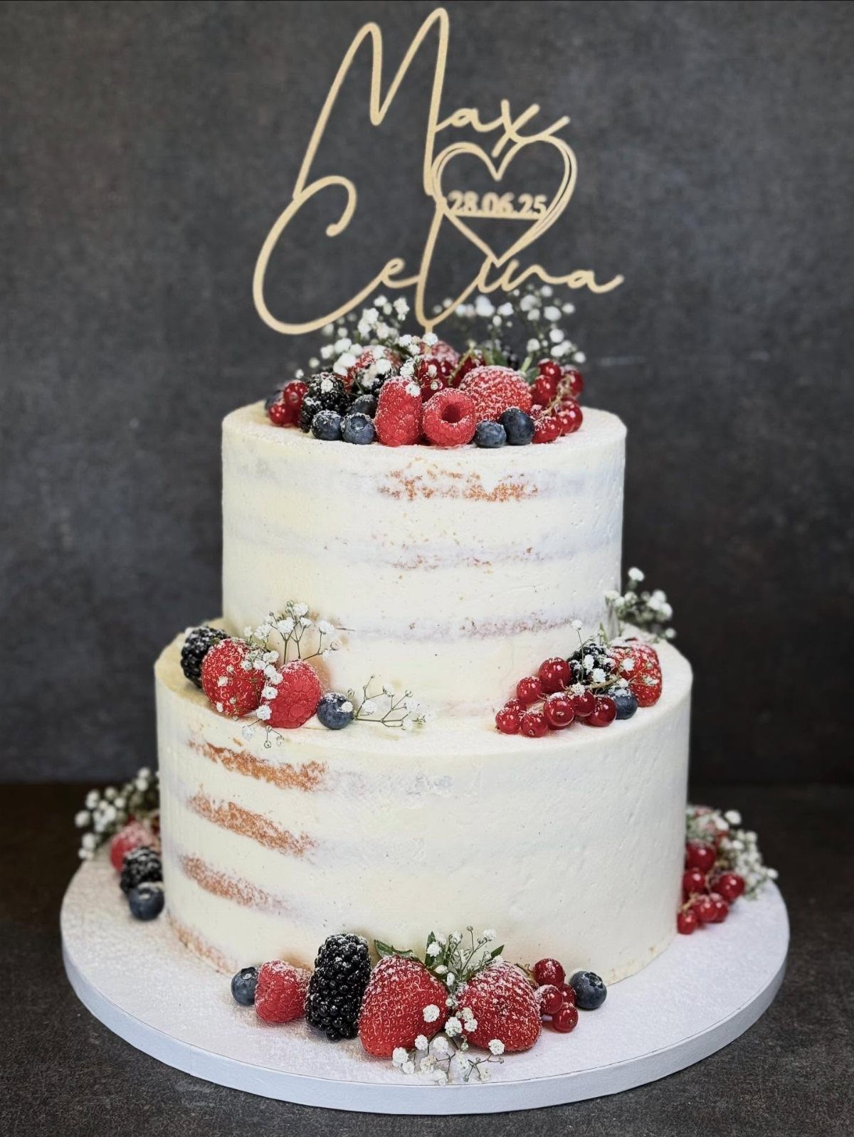 Two-tier semi-naked wedding cake decorated with fresh berries and white baby's breath flowers.