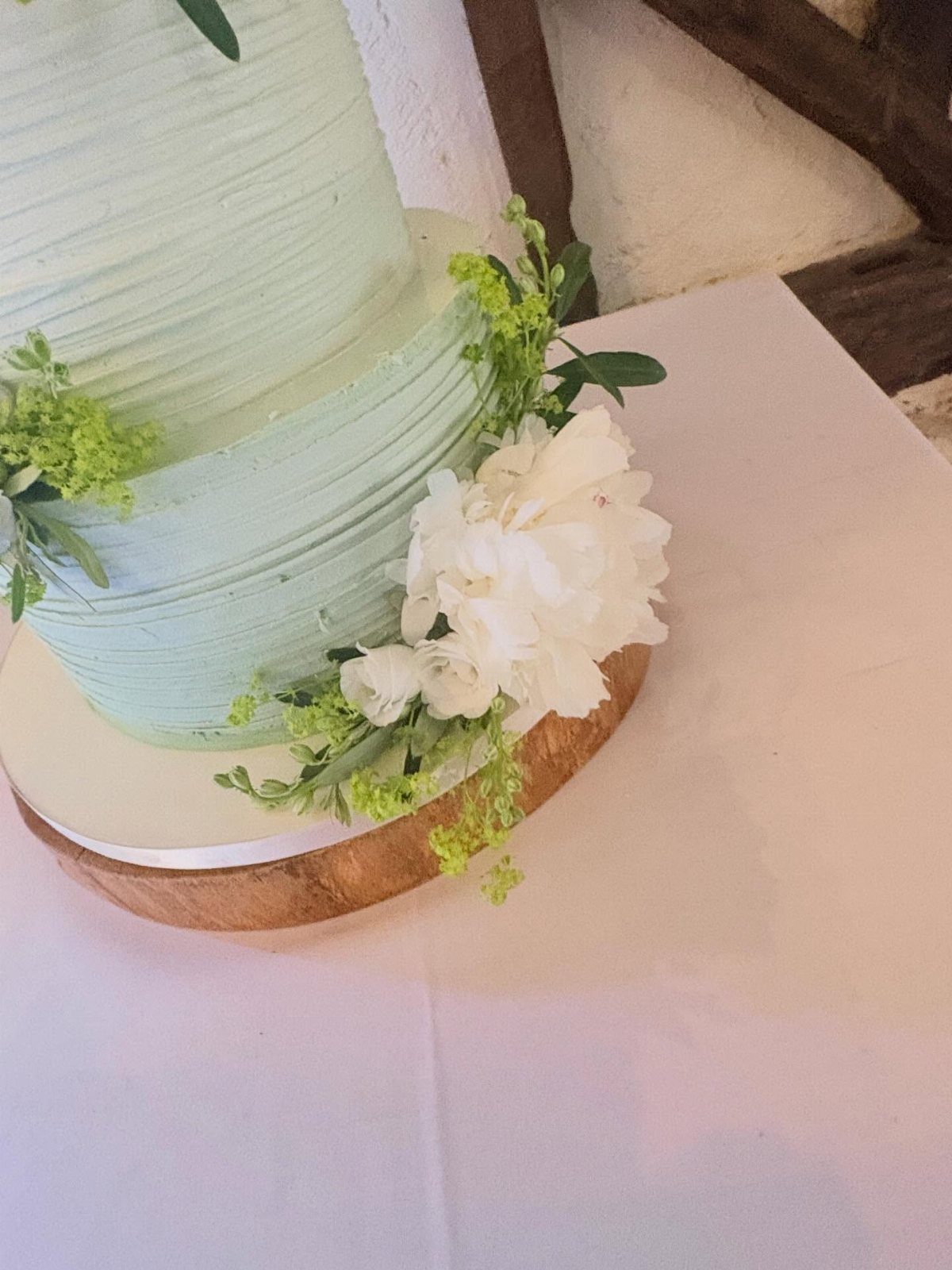 Mint green tiered wedding cake decorated with white flowers on a wooden stand