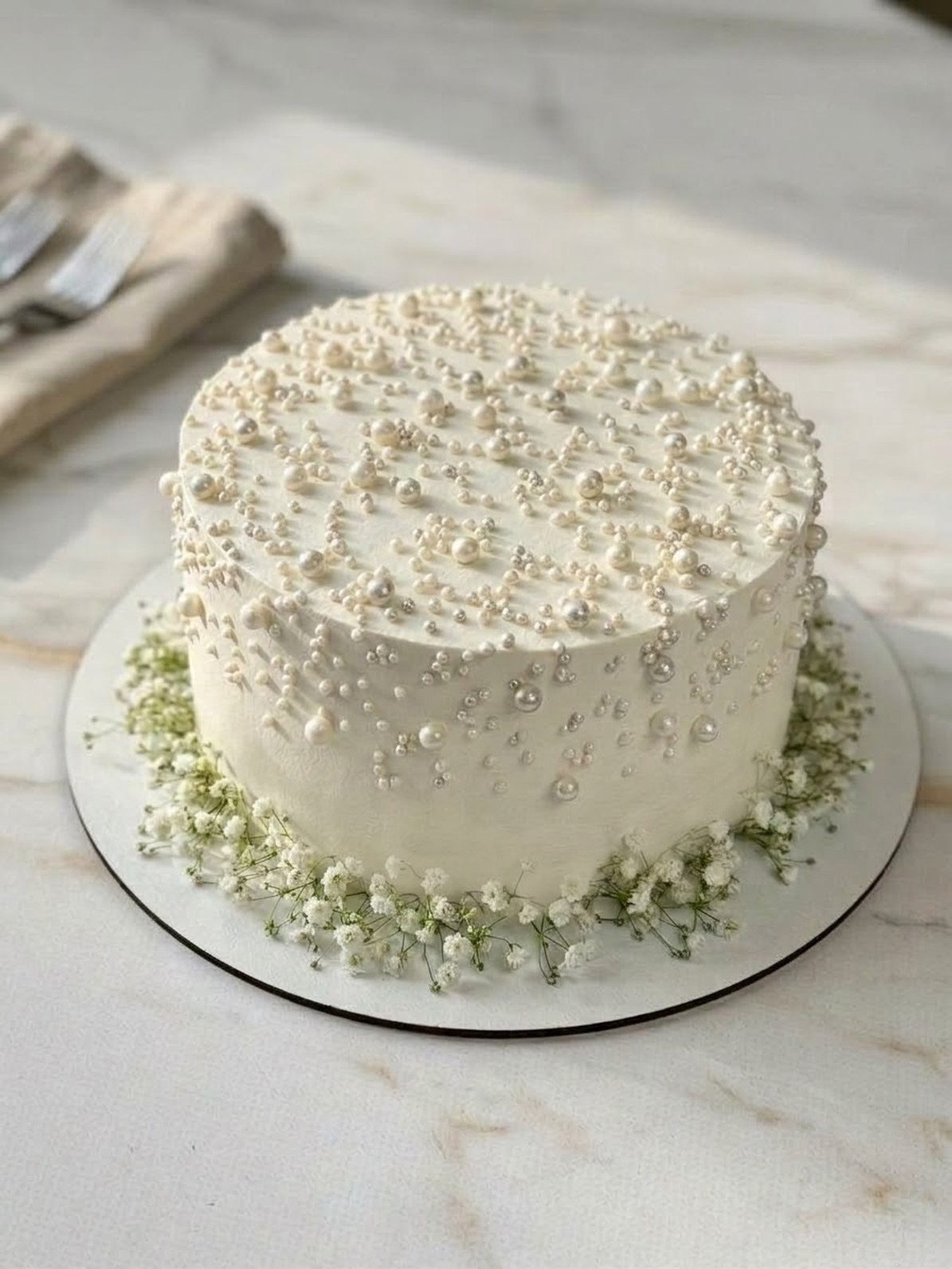 White frosted cake decorated with edible pearls and surrounded by baby's breath flowers.