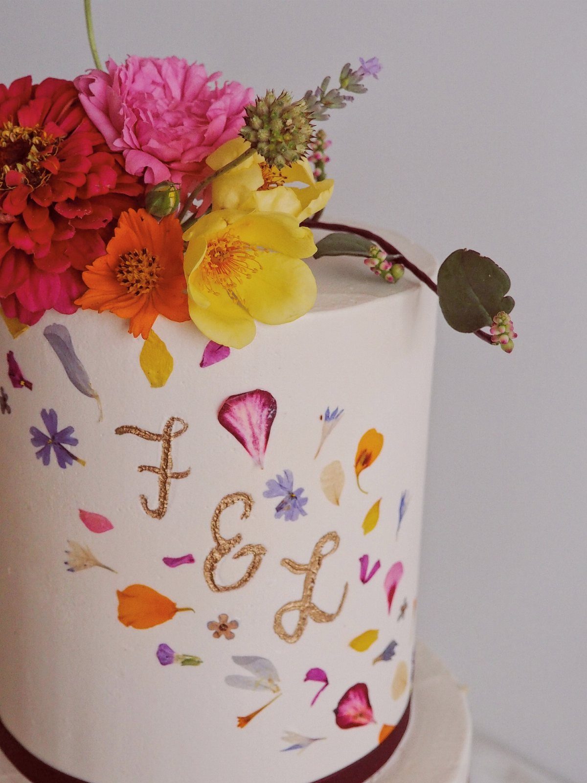 White wedding cake decorated with fresh colorful flowers and gold glitter initials