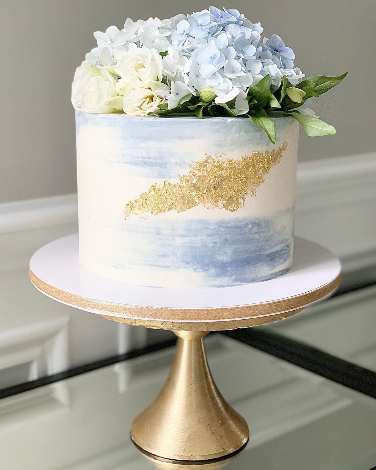 Watercolor painted cake with blue accents, gold foil, and fresh spring flowers