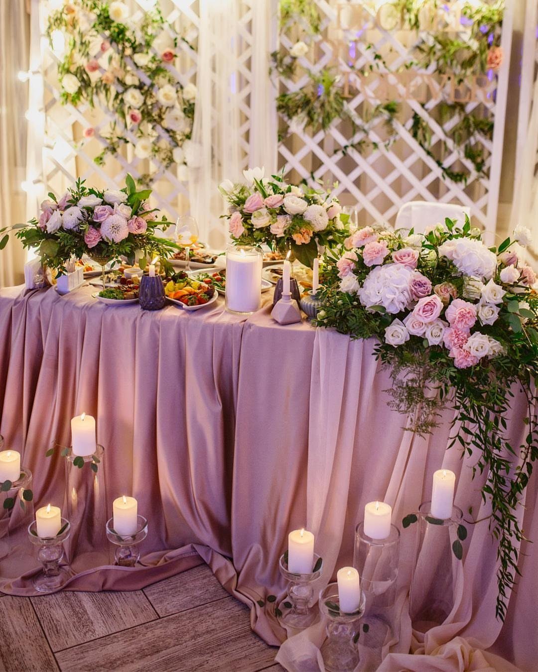 Dusty rose draped wedding table with pink floral arrangements and white pillar candles.