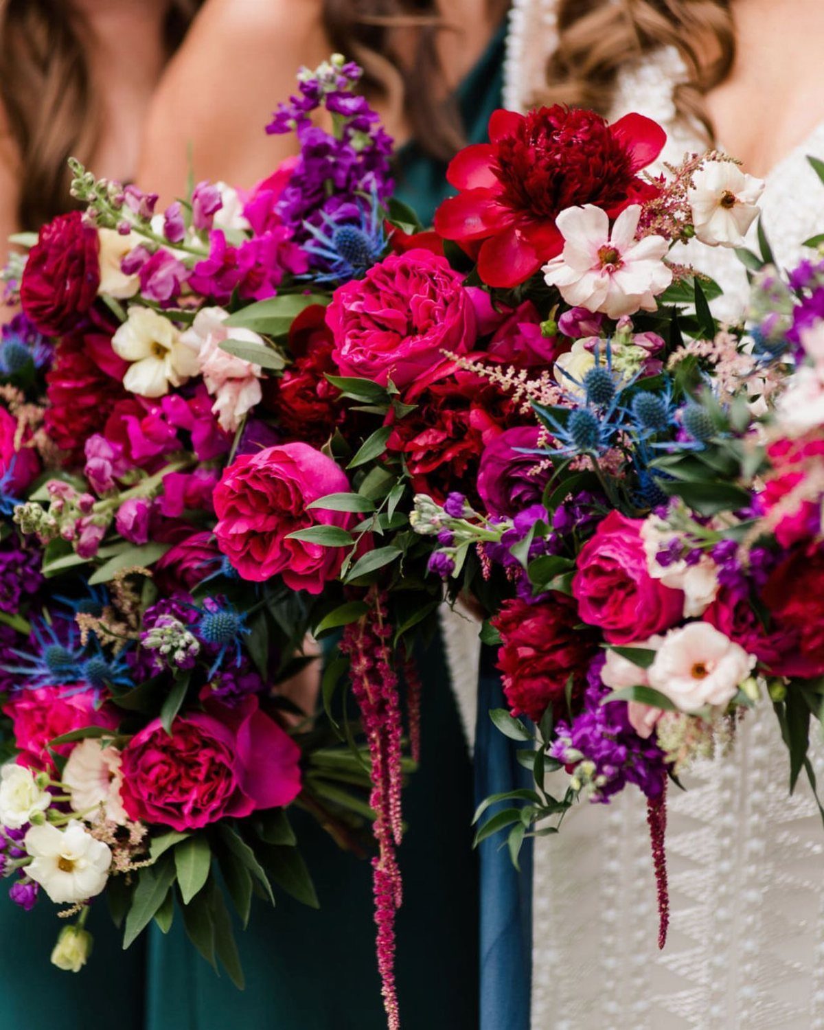 Bridal bouquets with burgundy peonies, pink roses, blue thistles, and emerald green foliage.