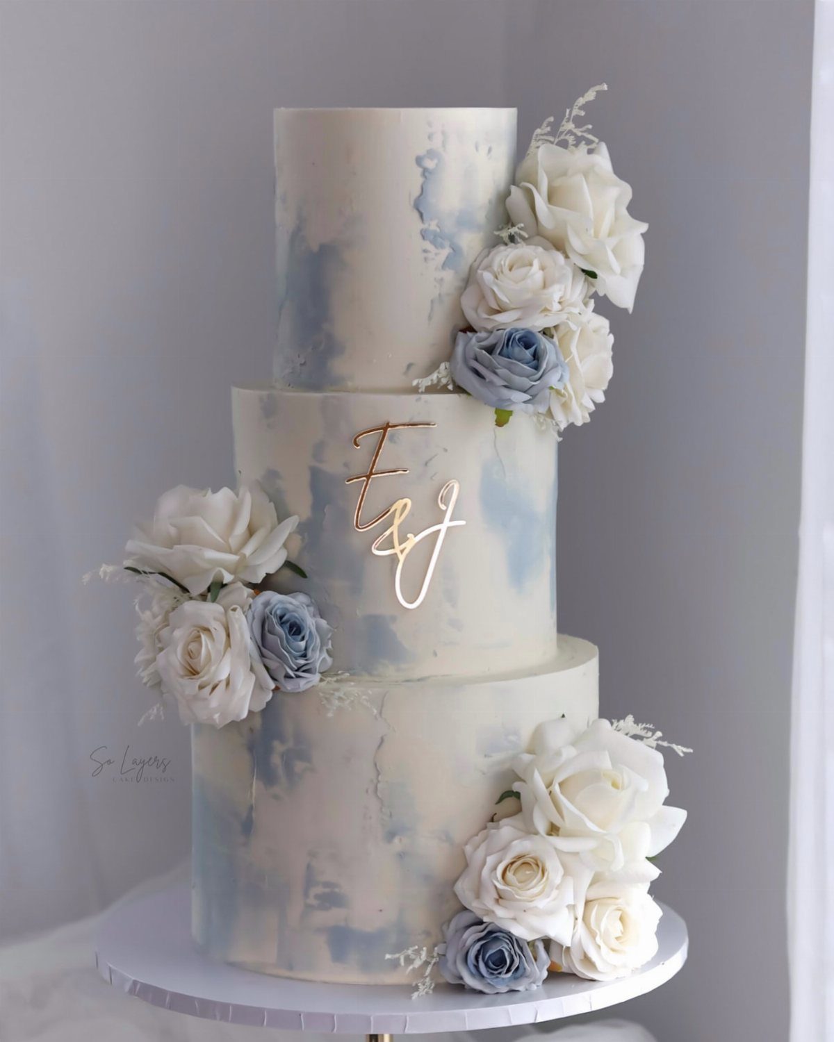 Three-tier white wedding cake with light blue watercolor accents and blue and white roses