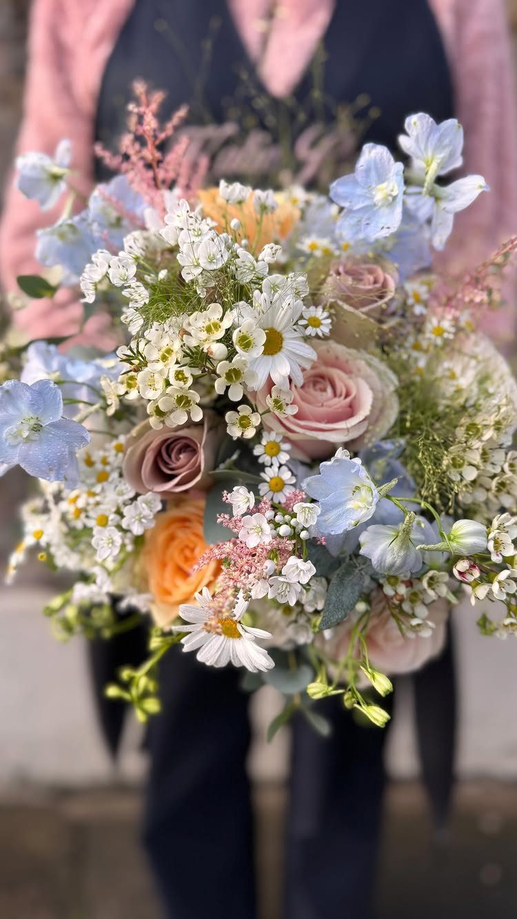 Bridal bouquet with pastel pink roses, light blue flowers, and white daisies.