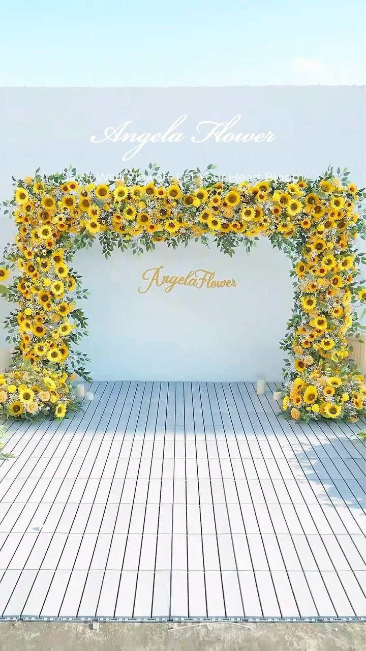 Sunflower and greenery floral arch against a white wall on a wooden deck