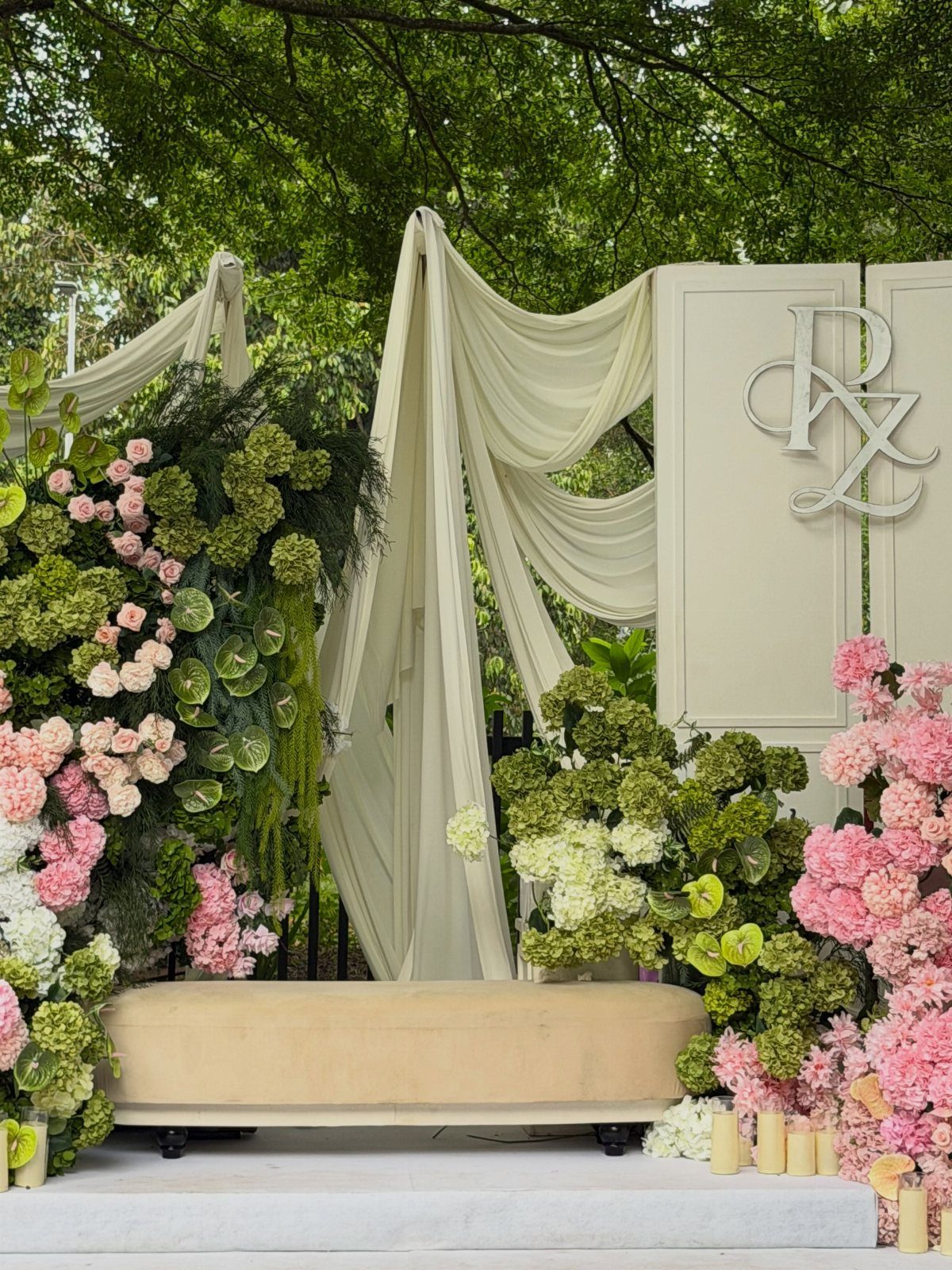 Wedding backdrop with vibrant pink and green floral arrangements and ivory fabric draping.