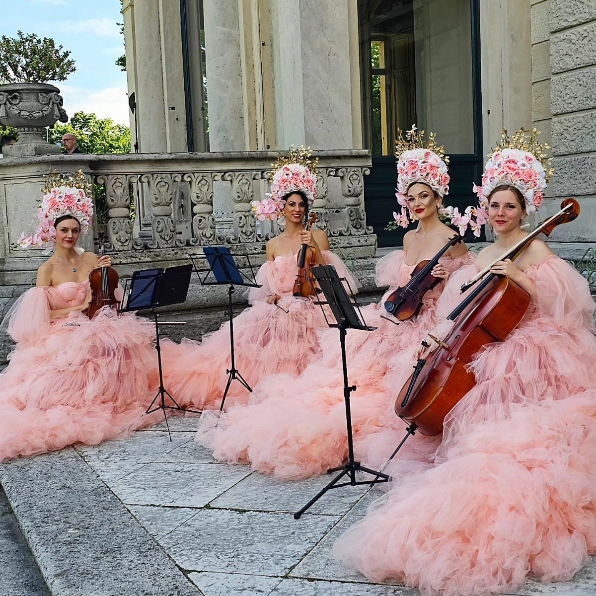 Four musicians in pink gowns playing a string quartet on a stone patio.