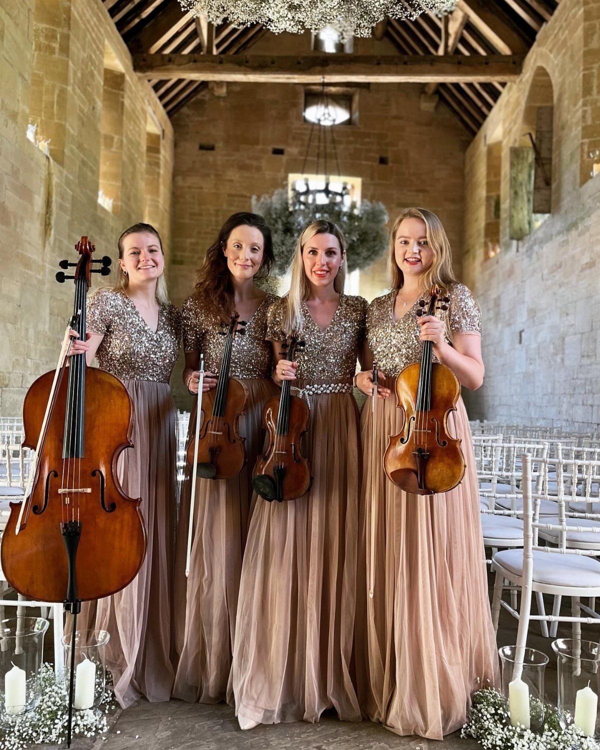 Four female musicians in gold gowns posing with string instruments in a chapel.