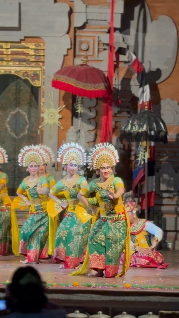 Balinese dancers in traditional green and gold costumes performing on a stage