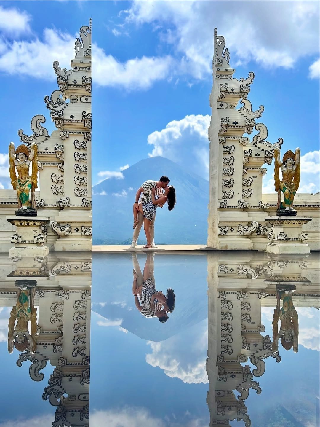 Couple kissing between ornate white Balinese gates reflected in a still water pool