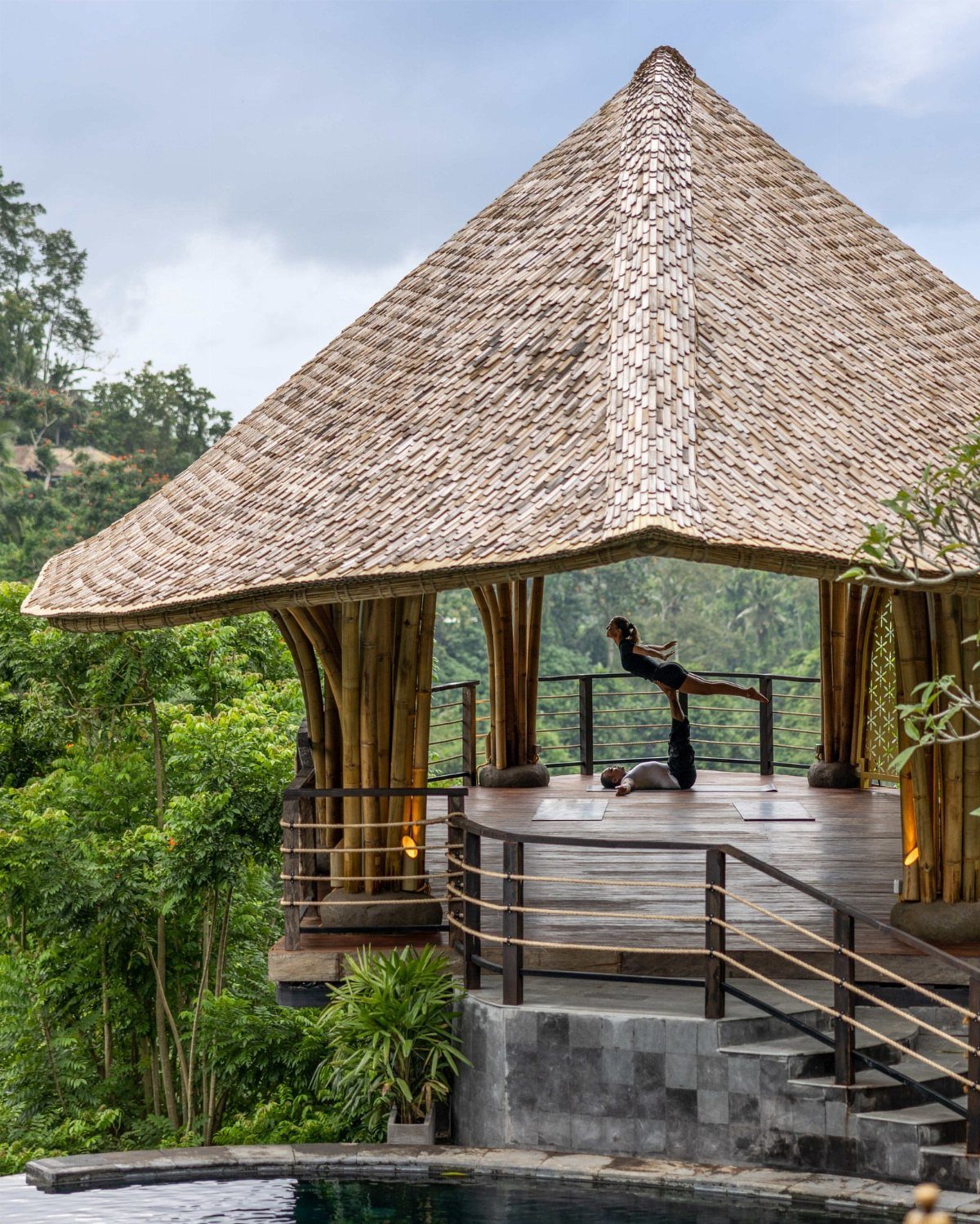 Woman practicing yoga on a wooden deck under a thatched pavilion in Ubud