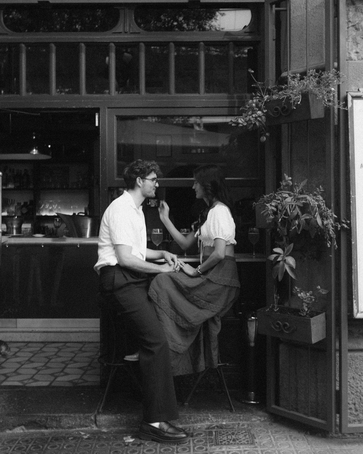 Couple in vintage clothing sitting at an outdoor cafe table in black and white