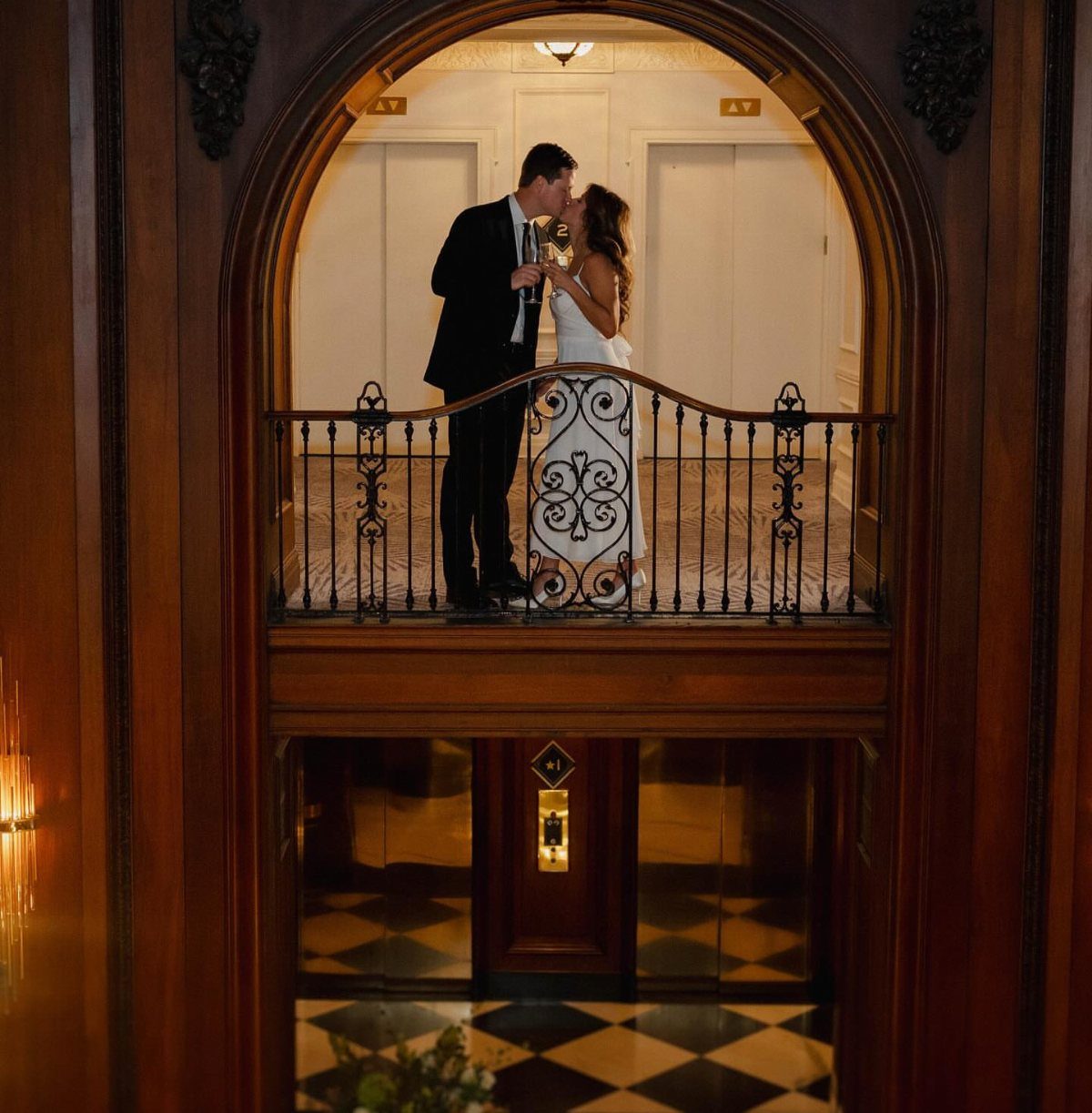 Couple kissing on a balcony framed by an ornate wooden archway in a historic building