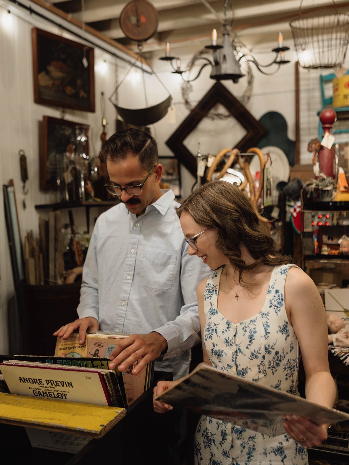 Couple browsing vinyl records inside a cluttered antique and thrift store.