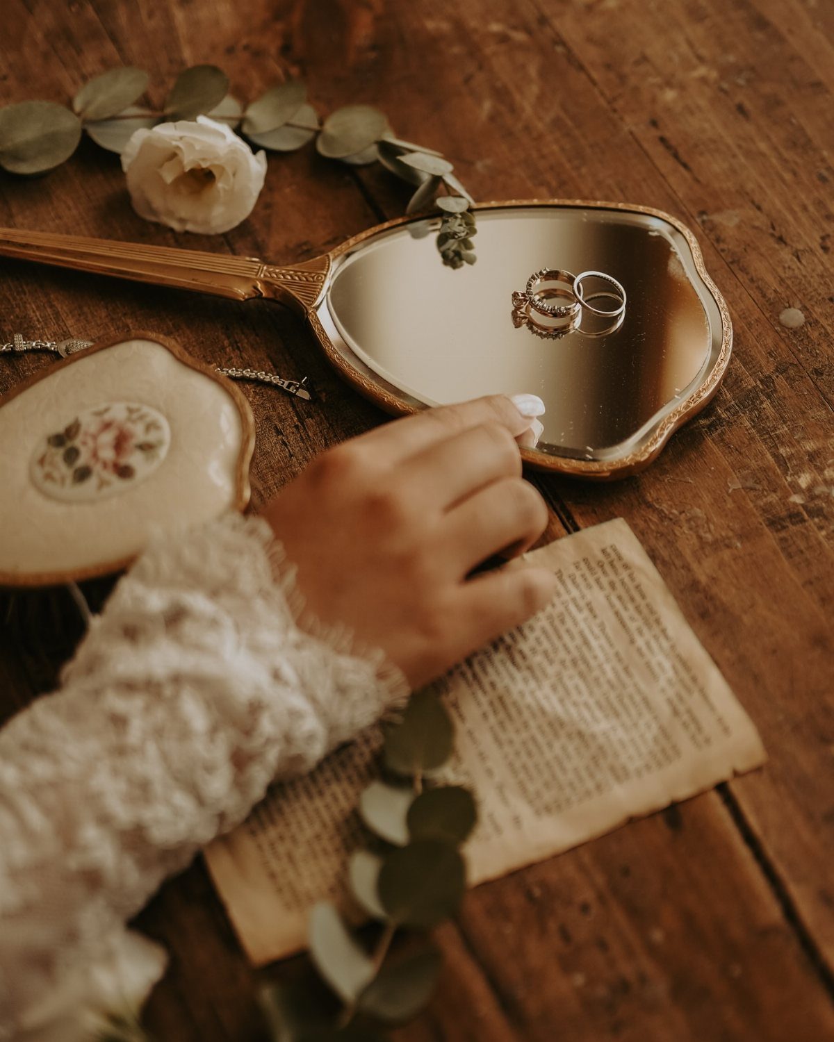 Engagement rings reflected in a vintage gold mirror next to a white rose.