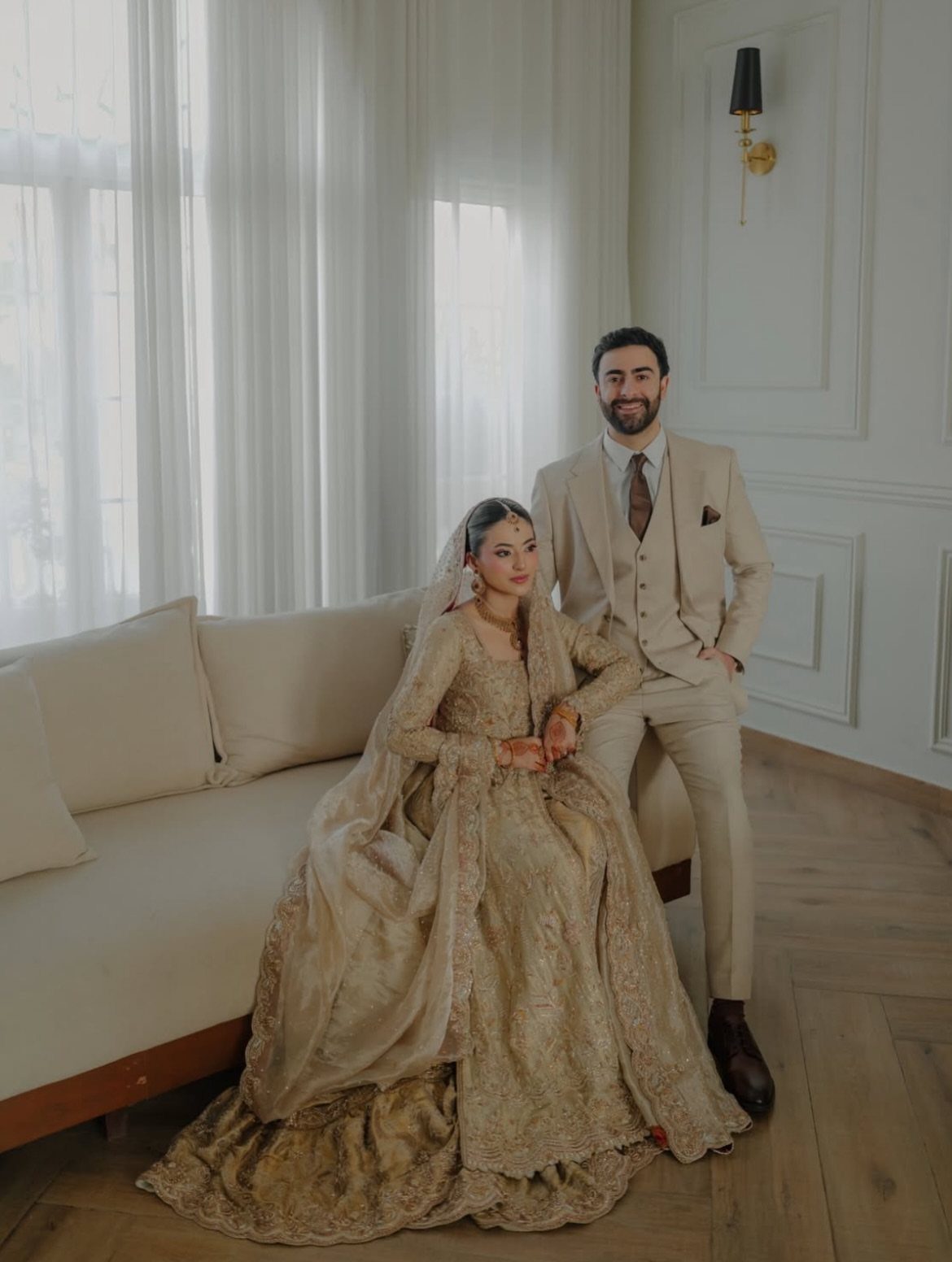 Couple in champagne-colored wedding attire posing in a bright, modern white room.