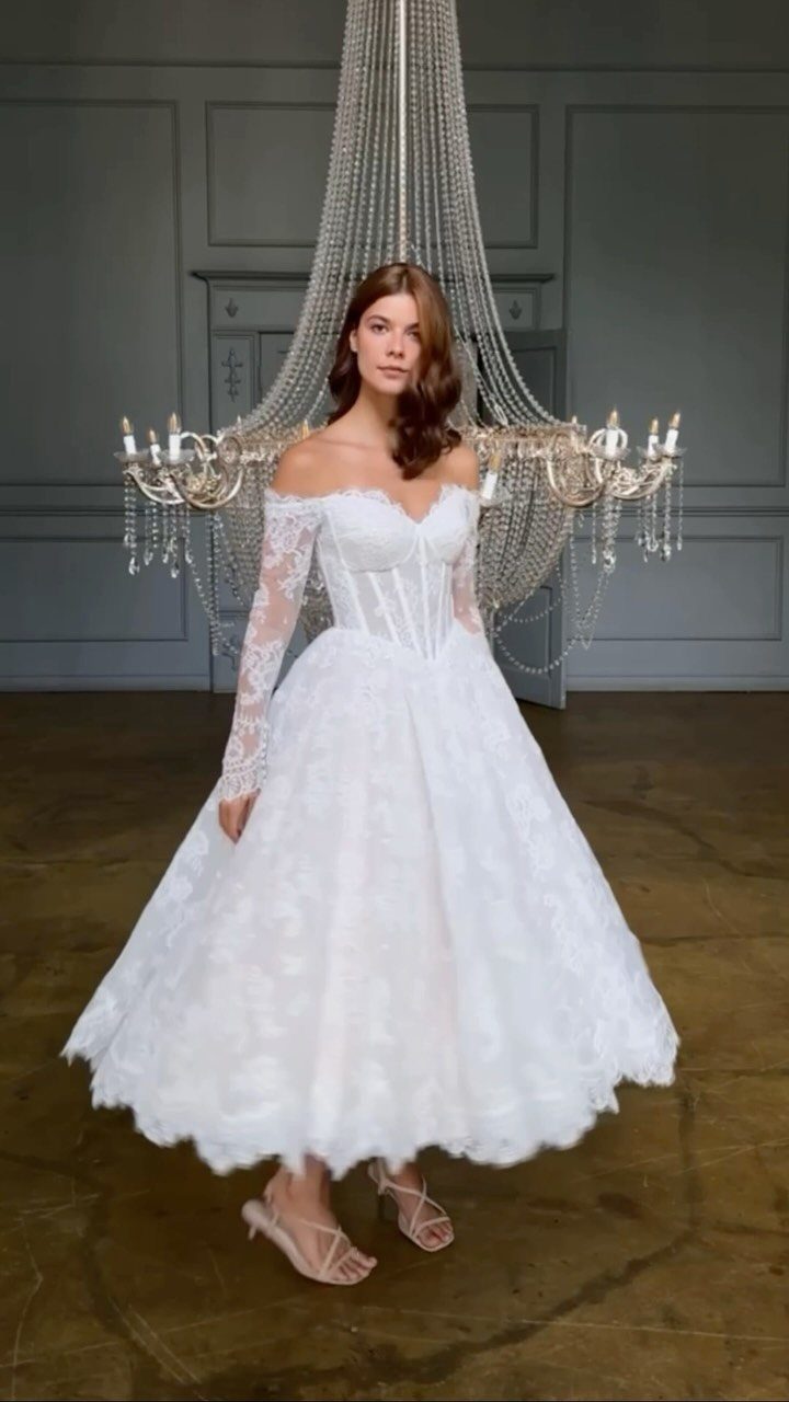 Woman in a white lace tea-length wedding dress standing before a crystal chandelier.