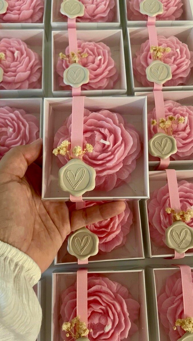 Pink flower-shaped candles in white boxes with ribbons and heart-shaped wax seals.