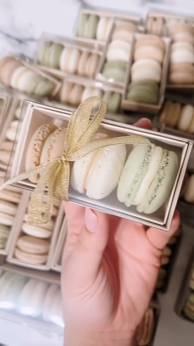 Three pastel macarons in a clear gift box tied with a gold ribbon.