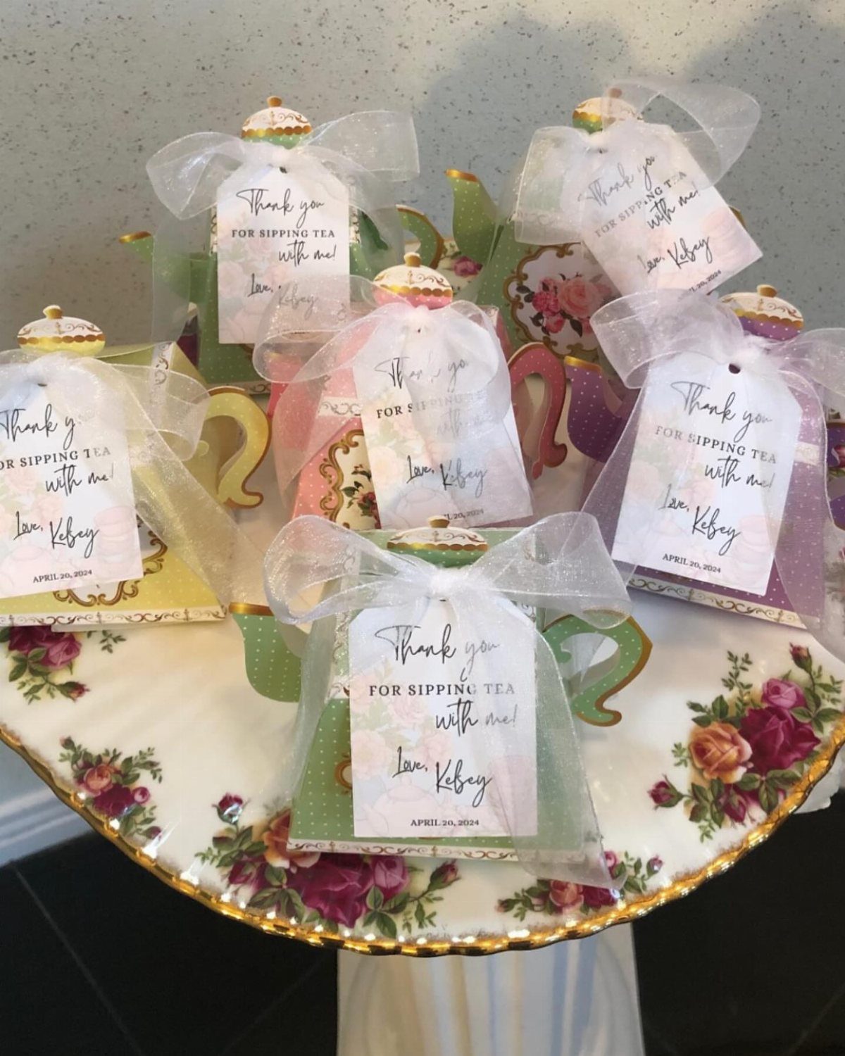 Small colorful teapots wrapped in tulle with thank you tags on floral stand