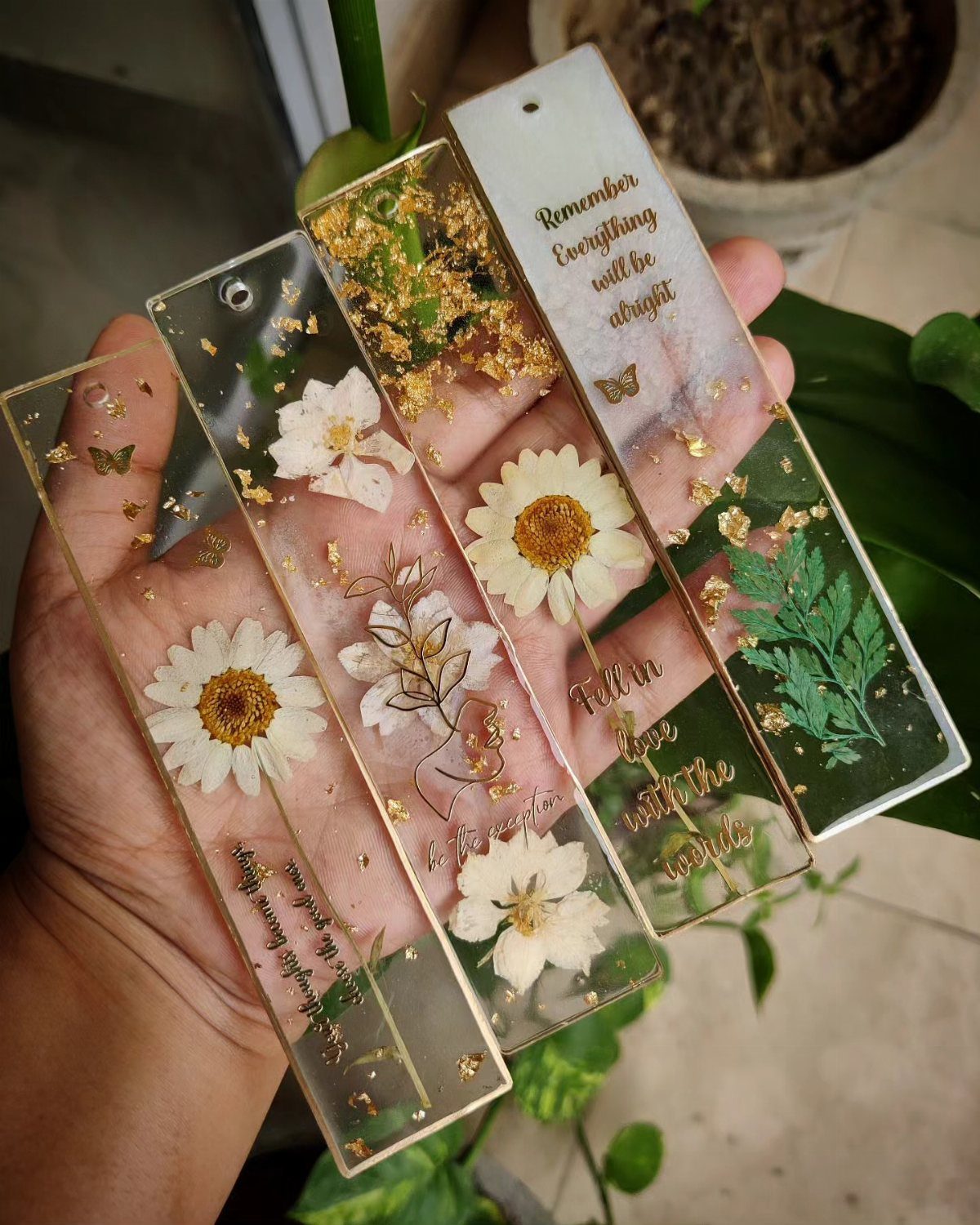 Pressed flower bookmarks made of clear resin with gold flakes held in a hand.