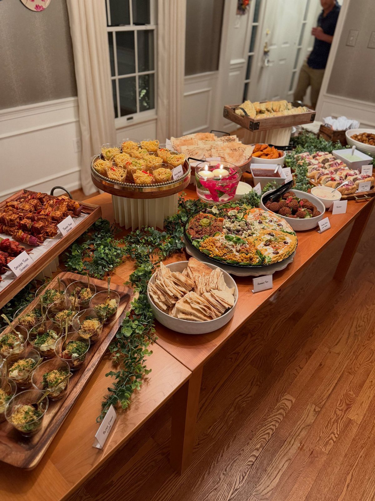 Catered appetizer spread on a wooden table with greenery and various party foods.