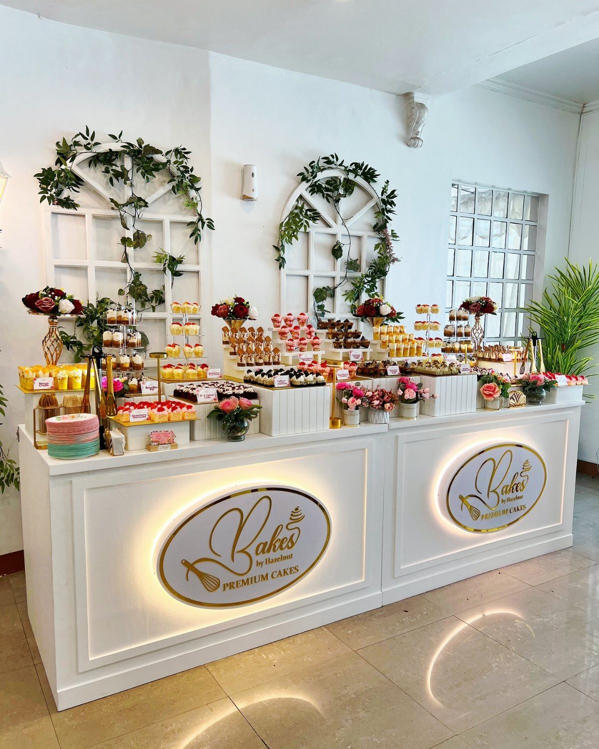 Dessert bar with assorted miniature cakes and pastries on a white illuminated table.