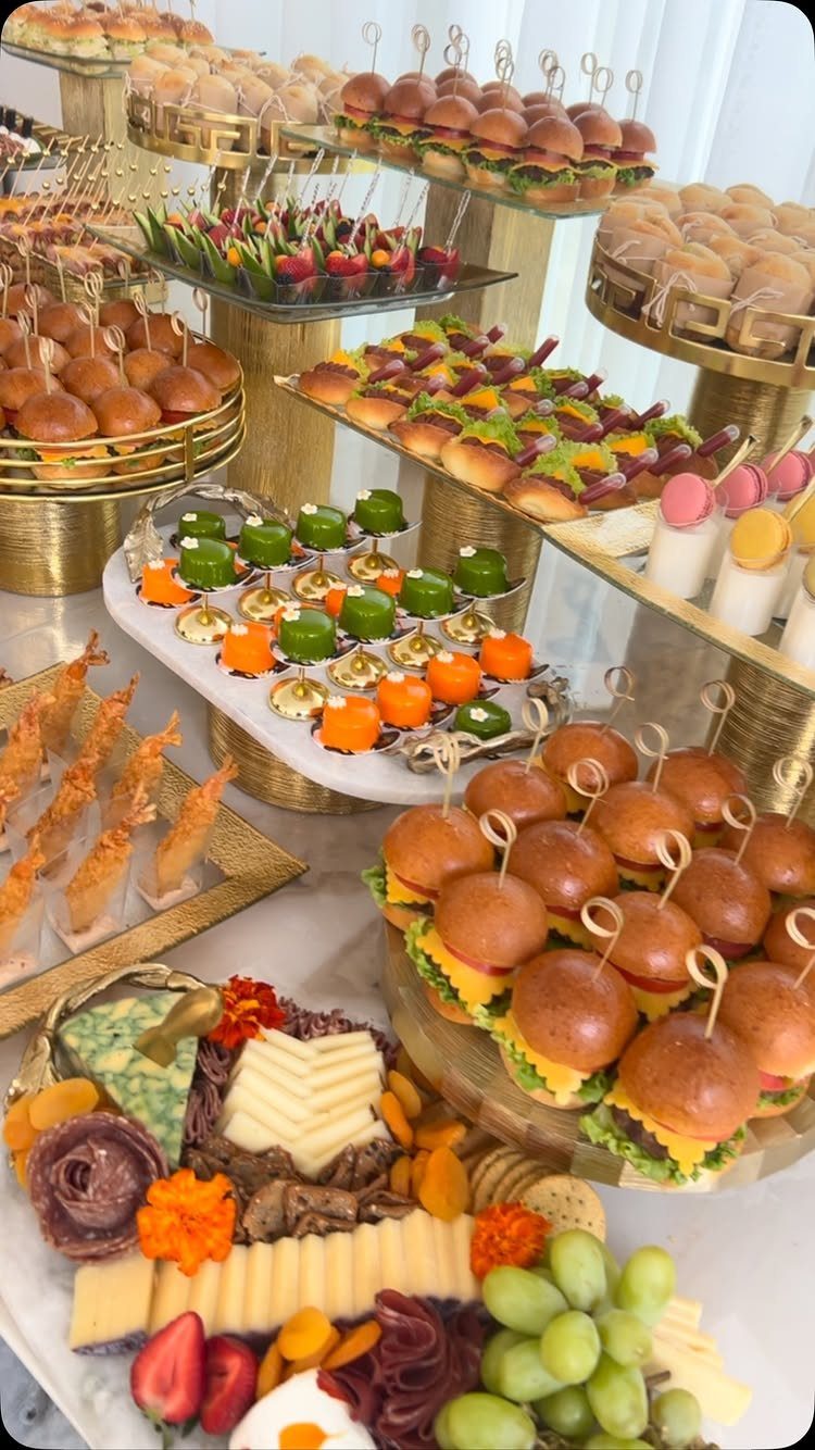 Lavish catering spread with mini burgers, cheese platters, and fruit on gold stands.