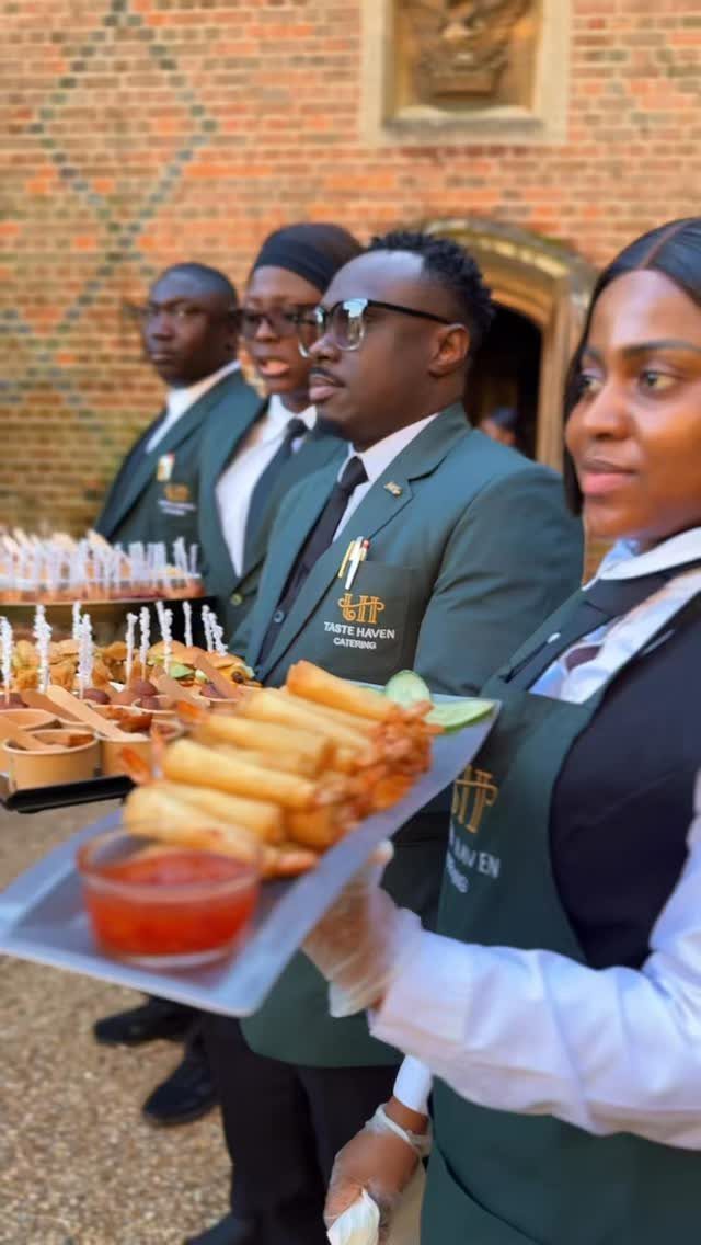 Servers in green uniforms holding trays of appetizers at an outdoor event