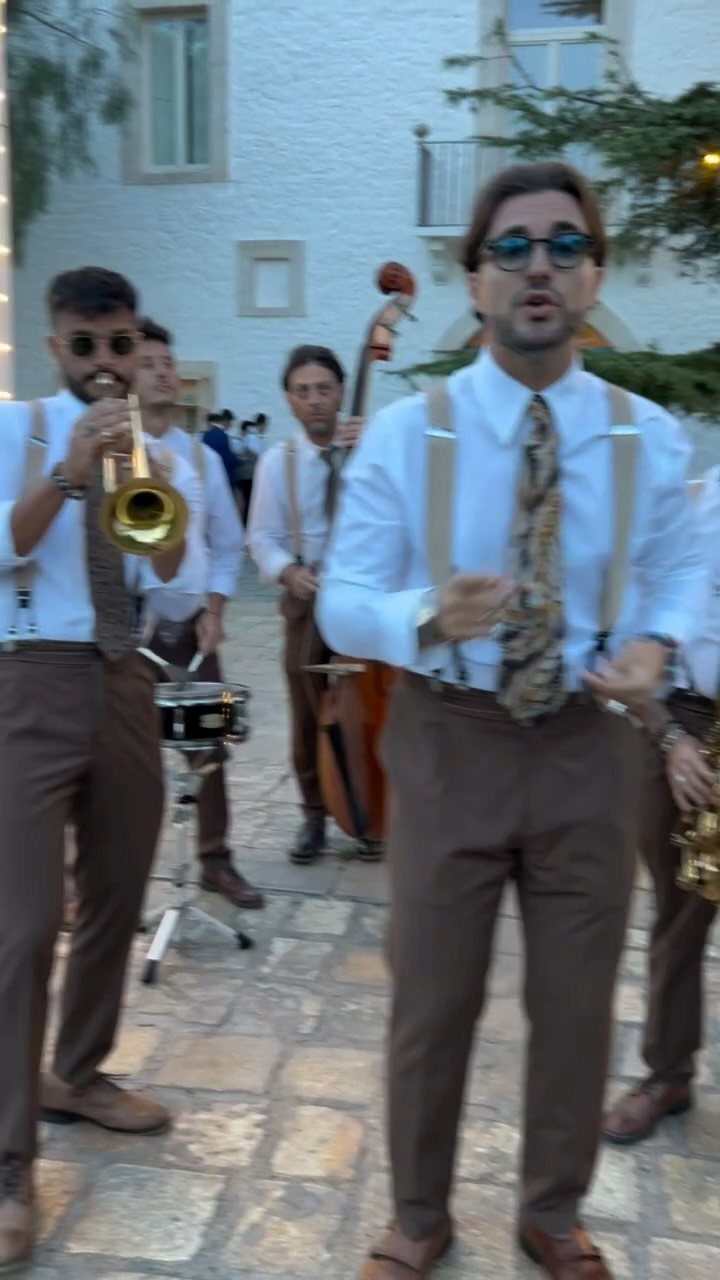 Musical band in white shirts and brown trousers performing outdoors on stone patio