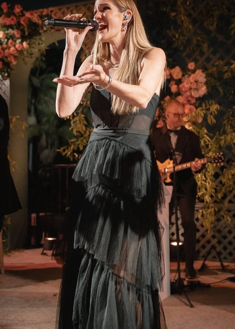 Female singer in a green dress performing with a guitarist at a wedding.
