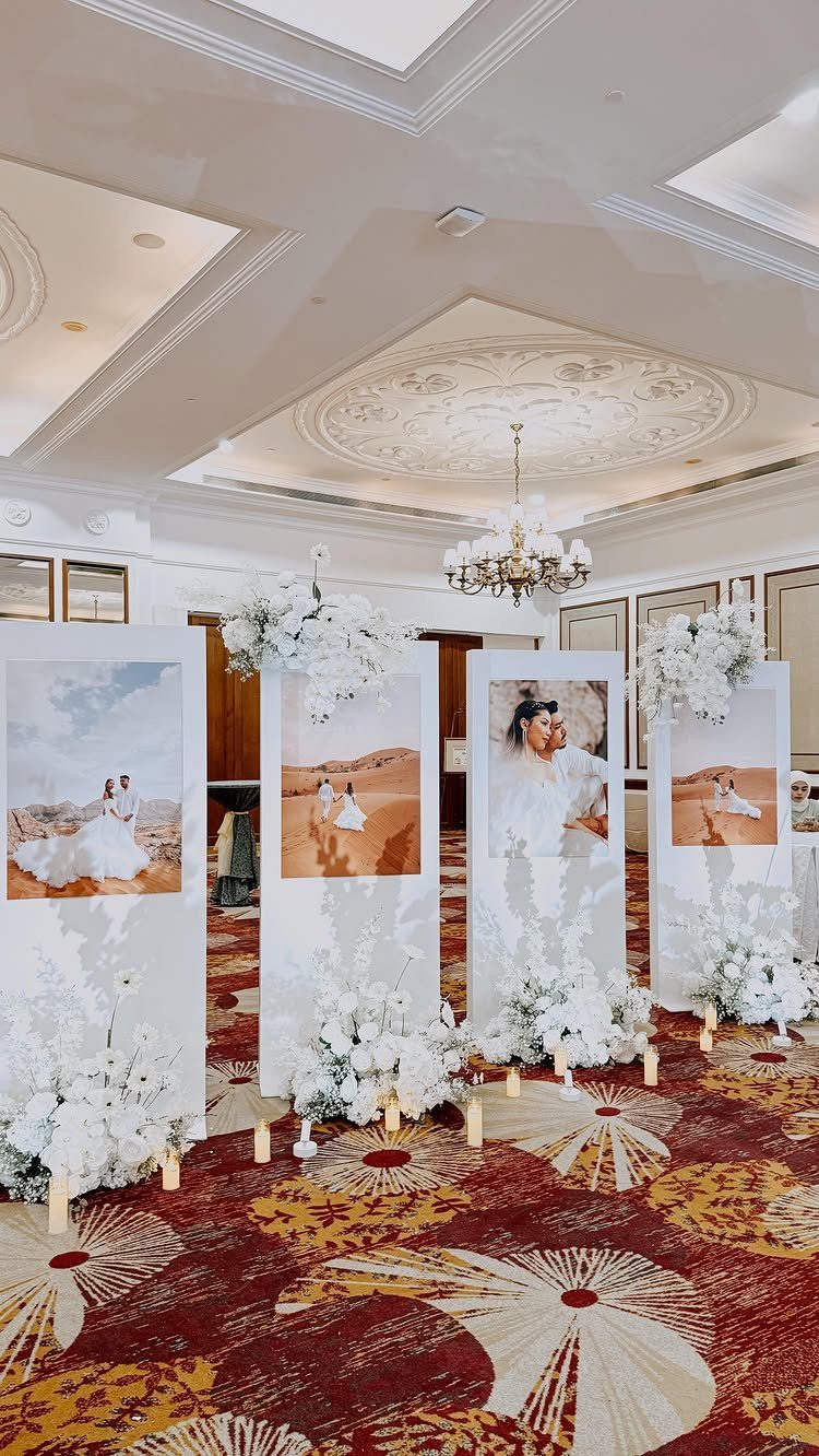 Wedding photographs displayed on large white panels with white floral arrangements in a ballroom