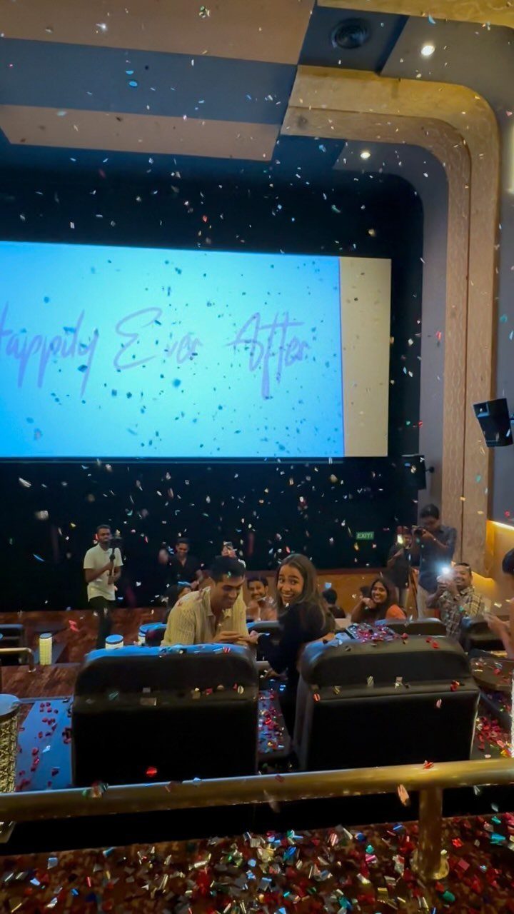Couple in a movie theater surrounded by confetti with a proposal message on screen