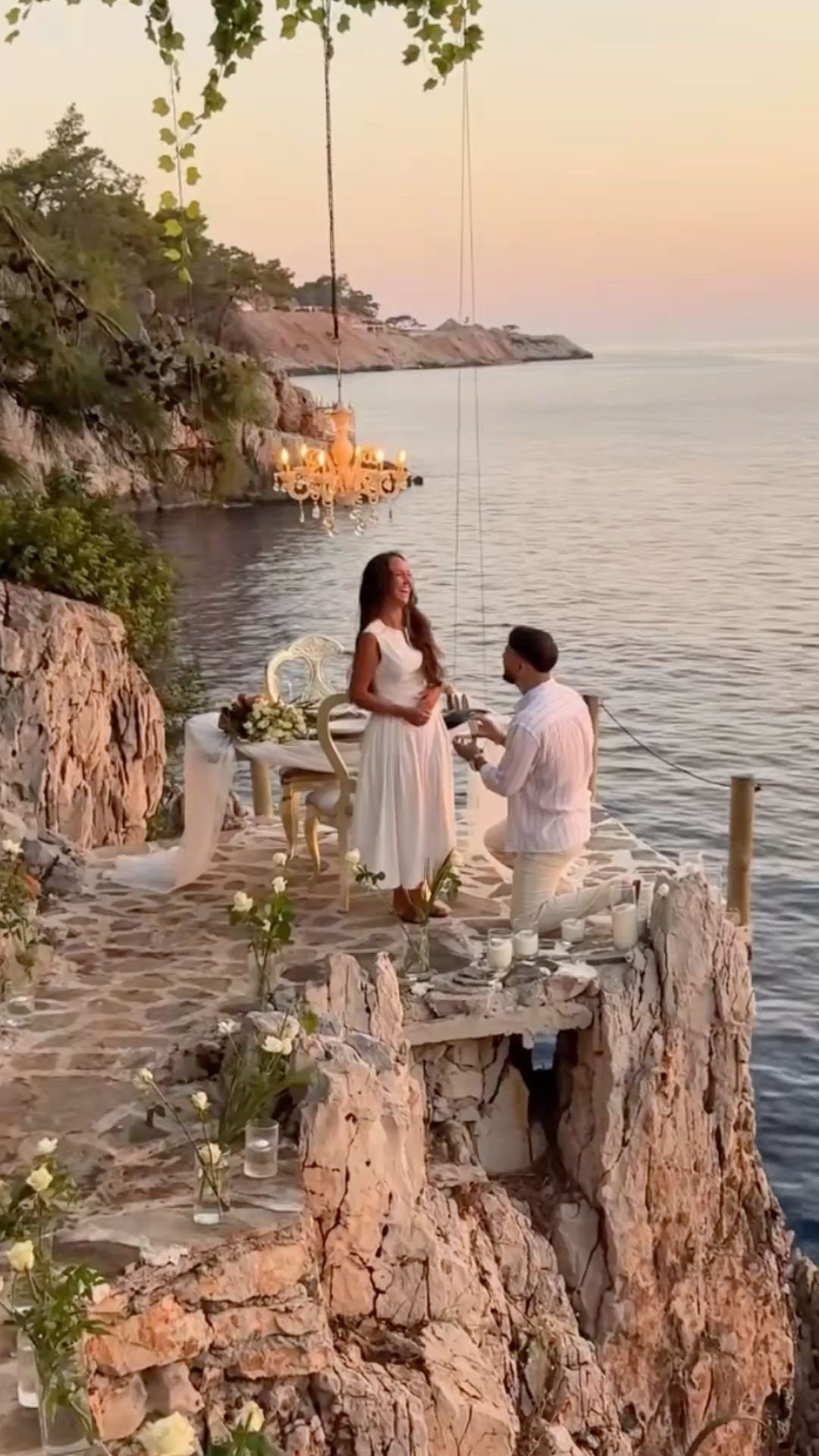 Man proposing to woman on a rocky cliff by the ocean at sunset