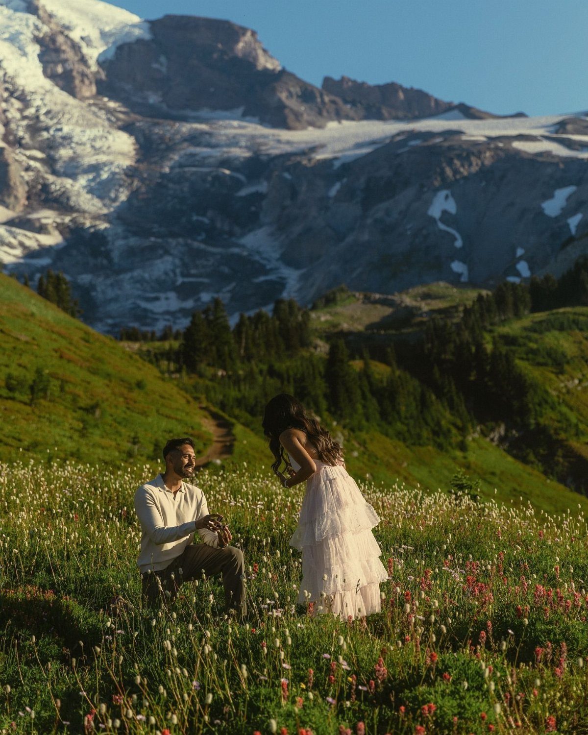 Man proposing to a woman in a wildflower meadow with mountains in background