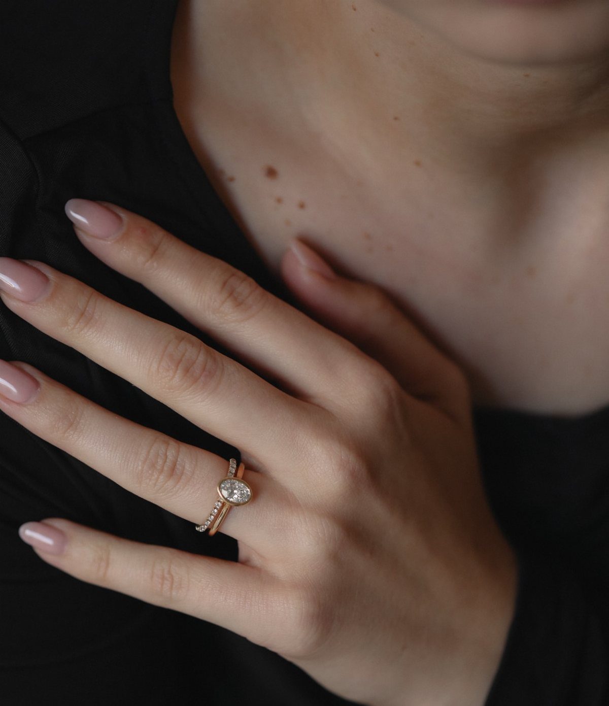 Gold wedding ring set with an oval diamond in a bezel setting on finger