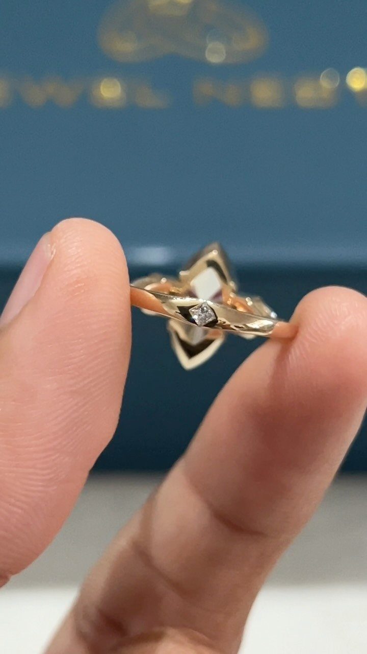 Gold ring with geometric design and small diamond held between two fingers