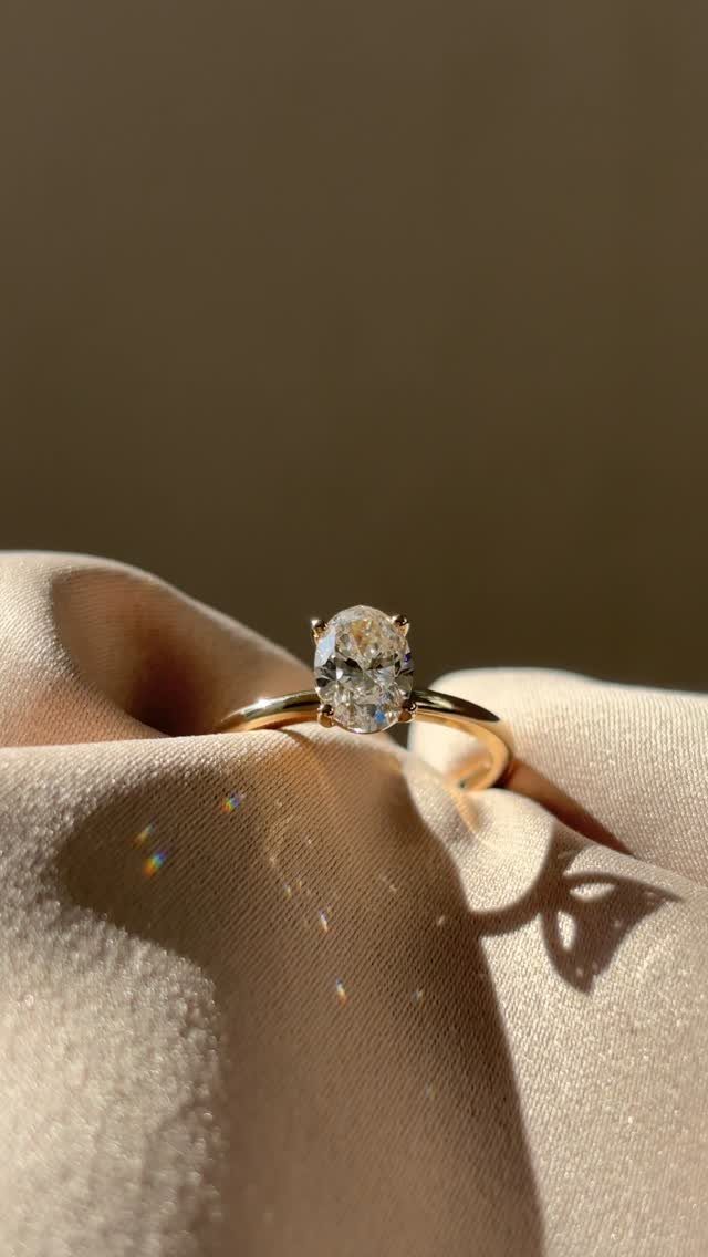 Gold ring with a single oval diamond resting on beige satin fabric.