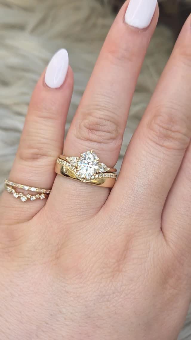 Gold three stone wedding ring set with oval center diamond on a finger