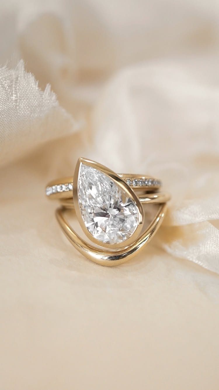 Gold wedding ring set with a pear-shaped diamond on cream fabric.