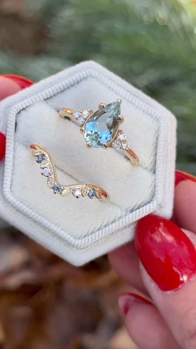 Two gold rings with light blue gemstones resting in a white hexagonal box.