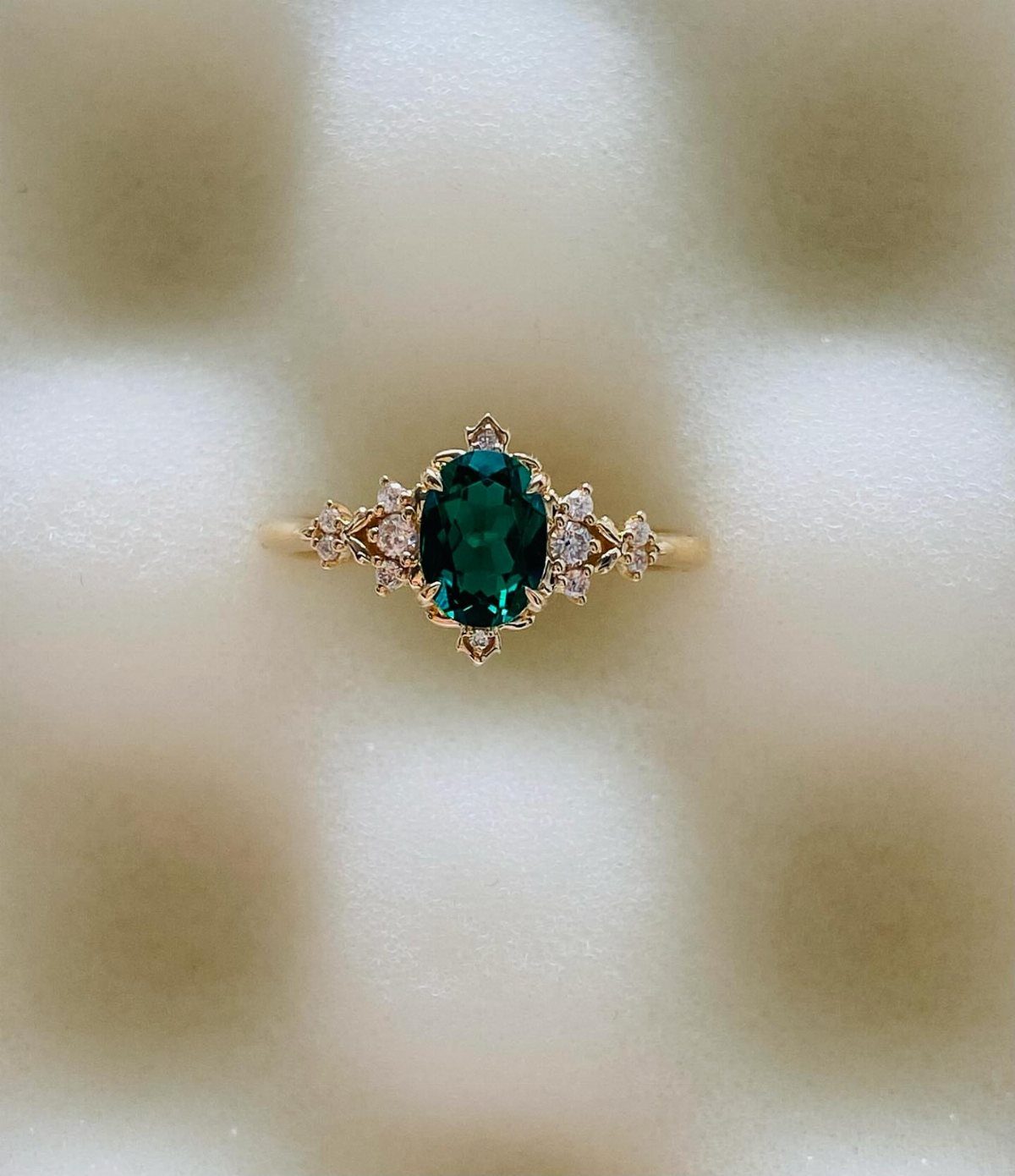 Gold ring with a central oval green emerald and small accent diamonds.