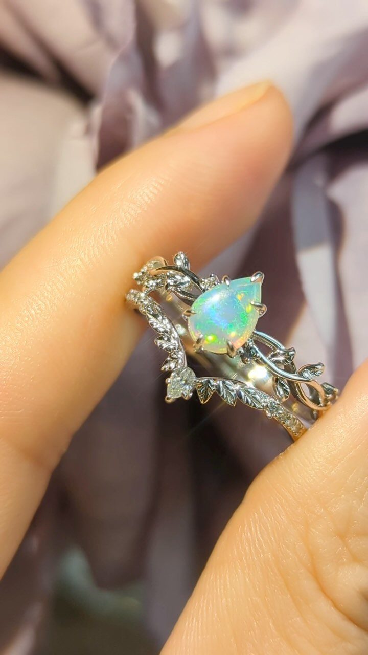 Pear-shaped iridescent opal wedding ring with leaf details on a finger