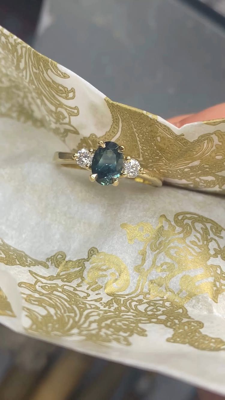 Gold ring with a dark blue oval sapphire and two small side diamonds.