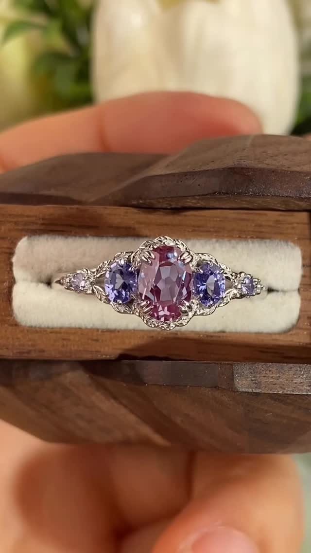 Silver wedding ring with a purple-blue tanzanite center stone in a wooden box.