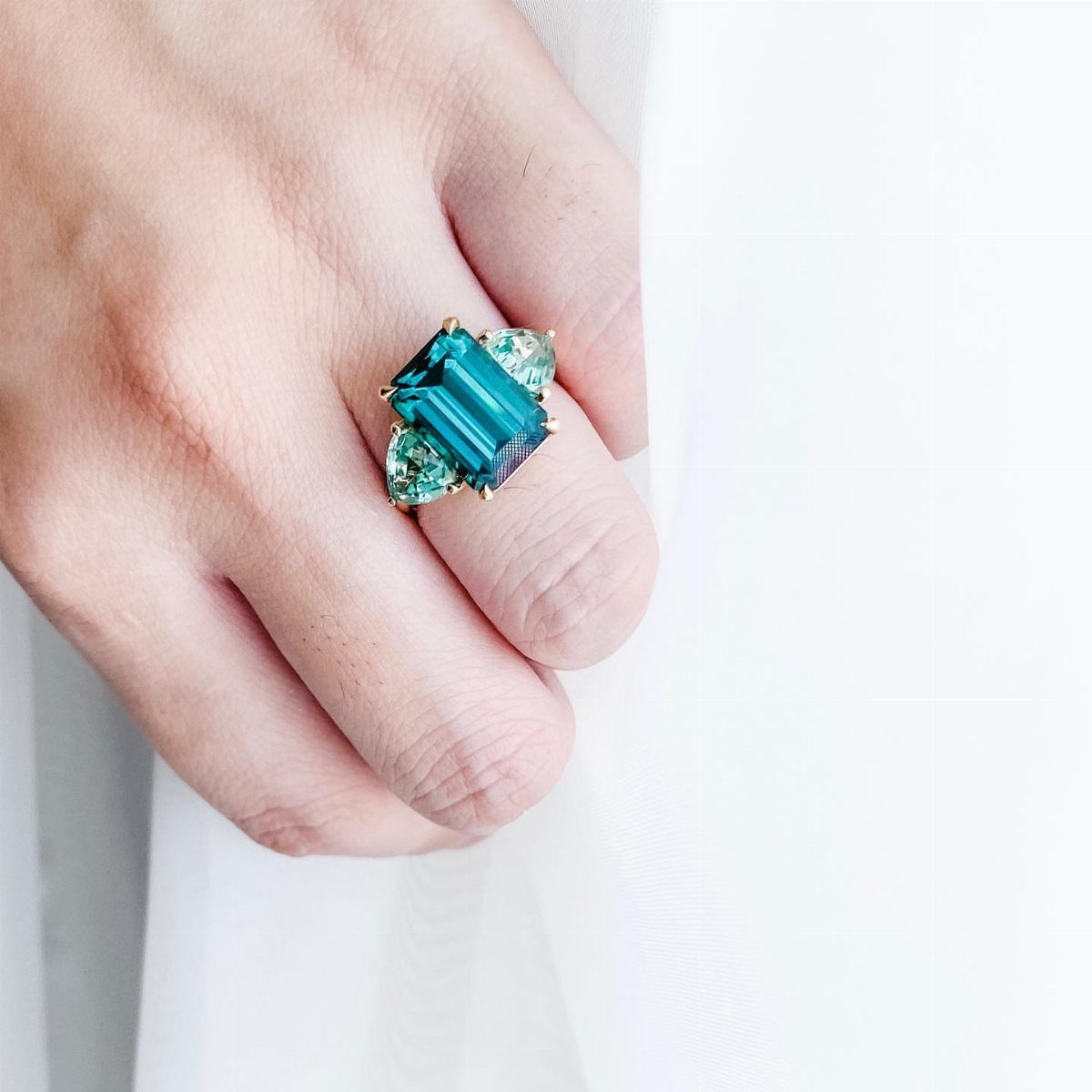 Gold ring with a teal emerald-cut gemstone worn on a person's finger